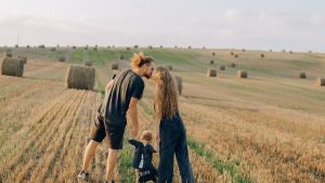 A couple with their child enjoy a sunny day in a wheat field, symbolizing love and joy.